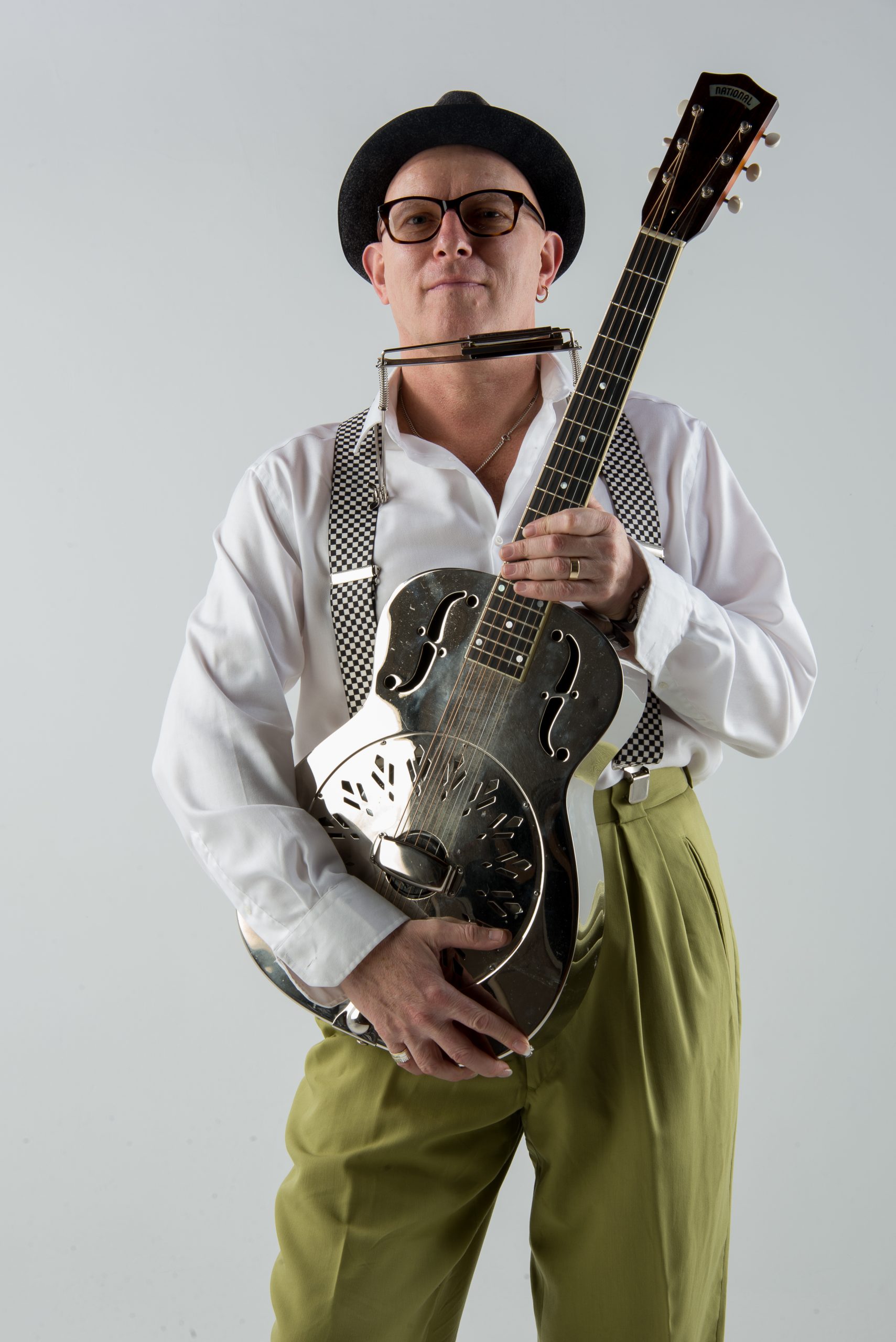 Eddie Martin trägt um den Hals einen Harmonica Holder und hält eine Gitarre in den Armen
