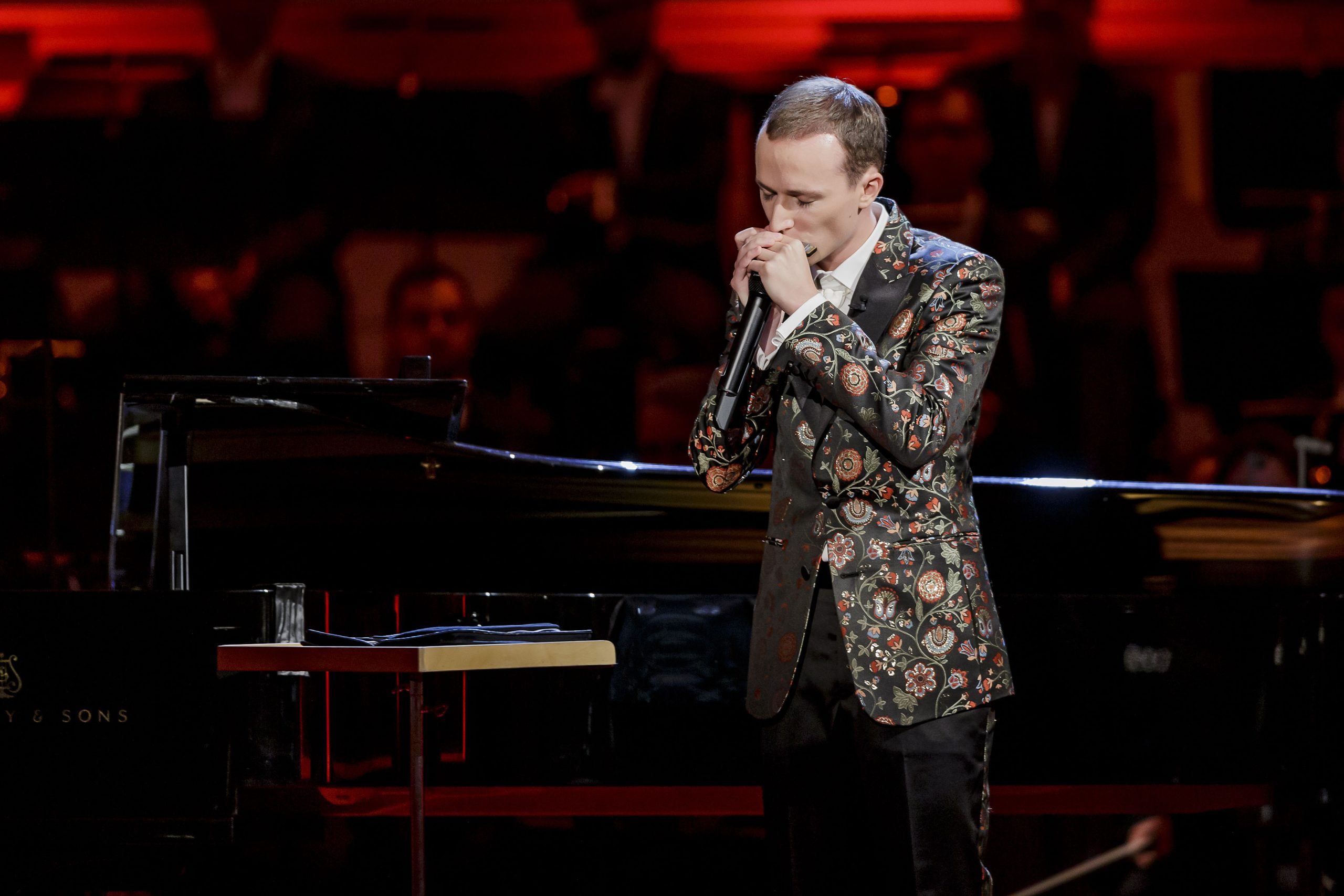 Konstantin Reinfeld spielt die Mundharmonika, im Hintergrund ist ein Flügel und Publikum zu sehen