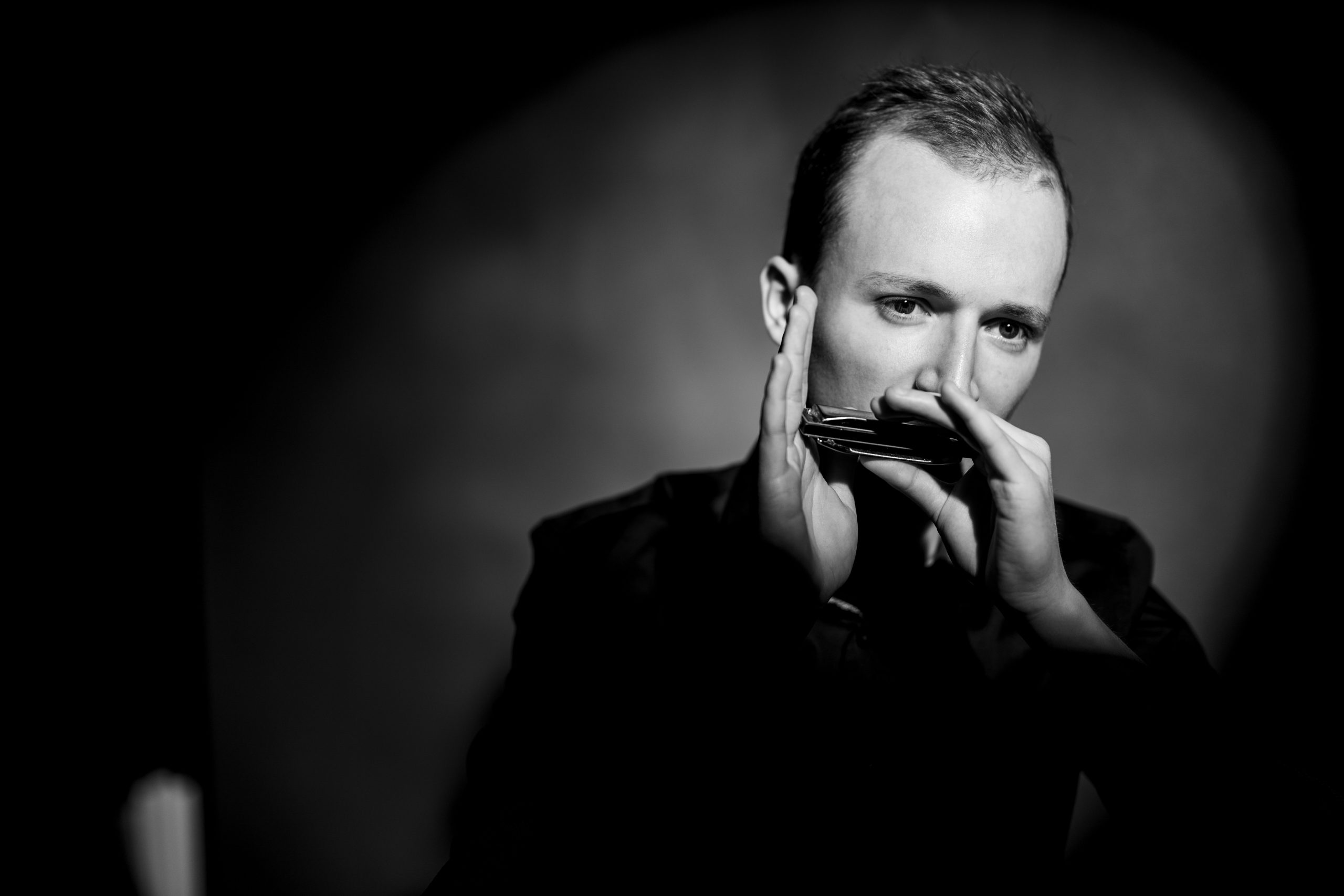 Konstantin Reinfeld in schwarz weiß der eine Mundharmonika spielt