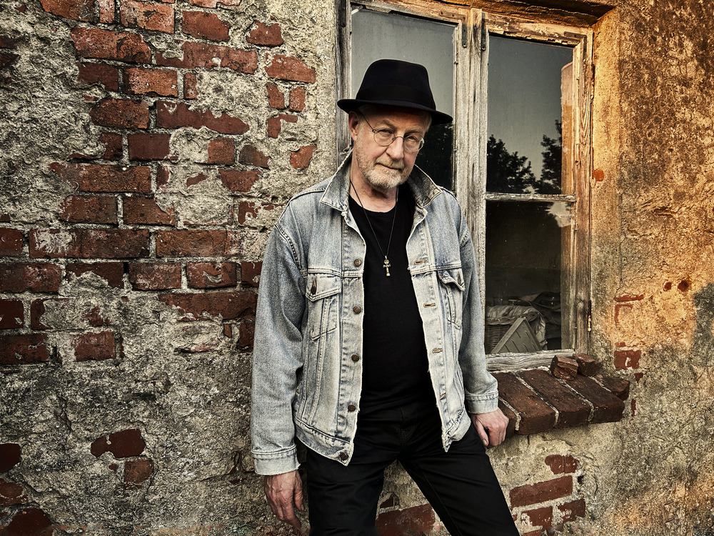 Musiker Steve Baker, der vor einer Ziegelwand steht