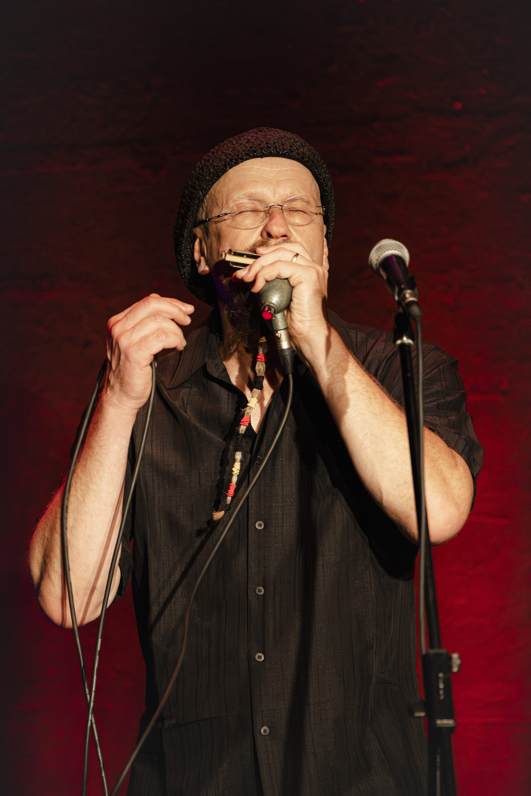 Joe Filisco auf der Bühne vor einem Mikrofon der eine Blues- Harp spielt