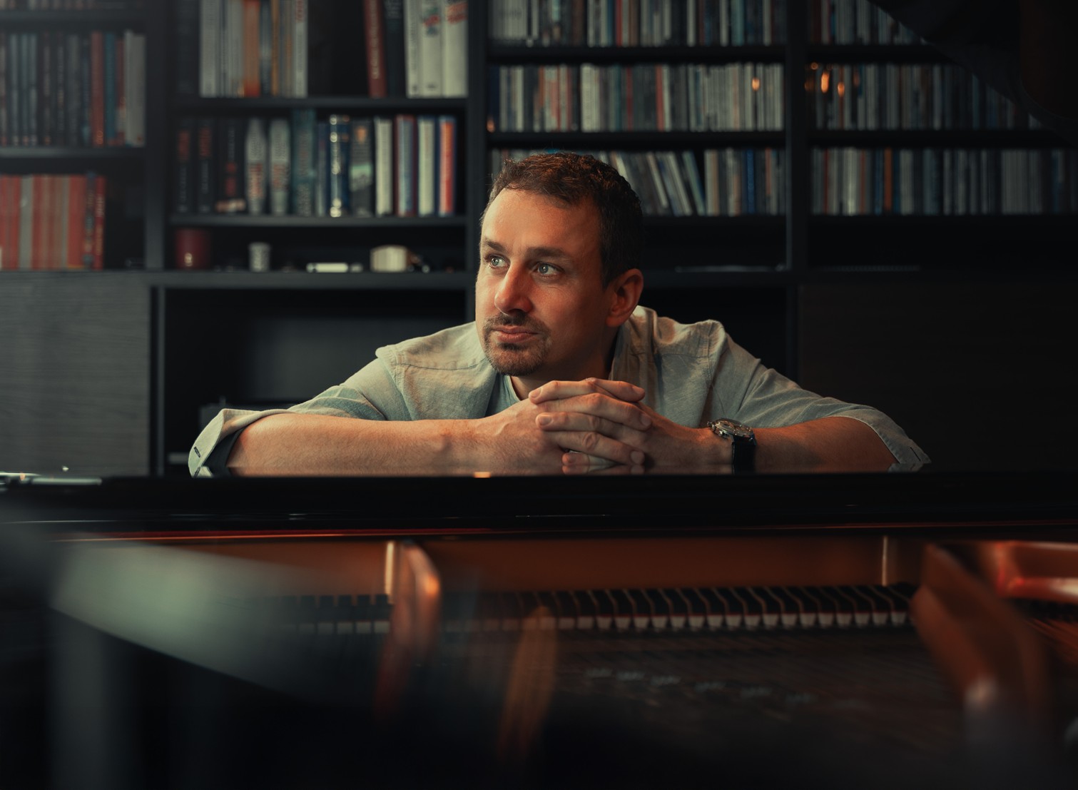 Musiker Thomas Förster der an einem Flügel sitzt und im Hintergrund ist eine großes Bücherregal