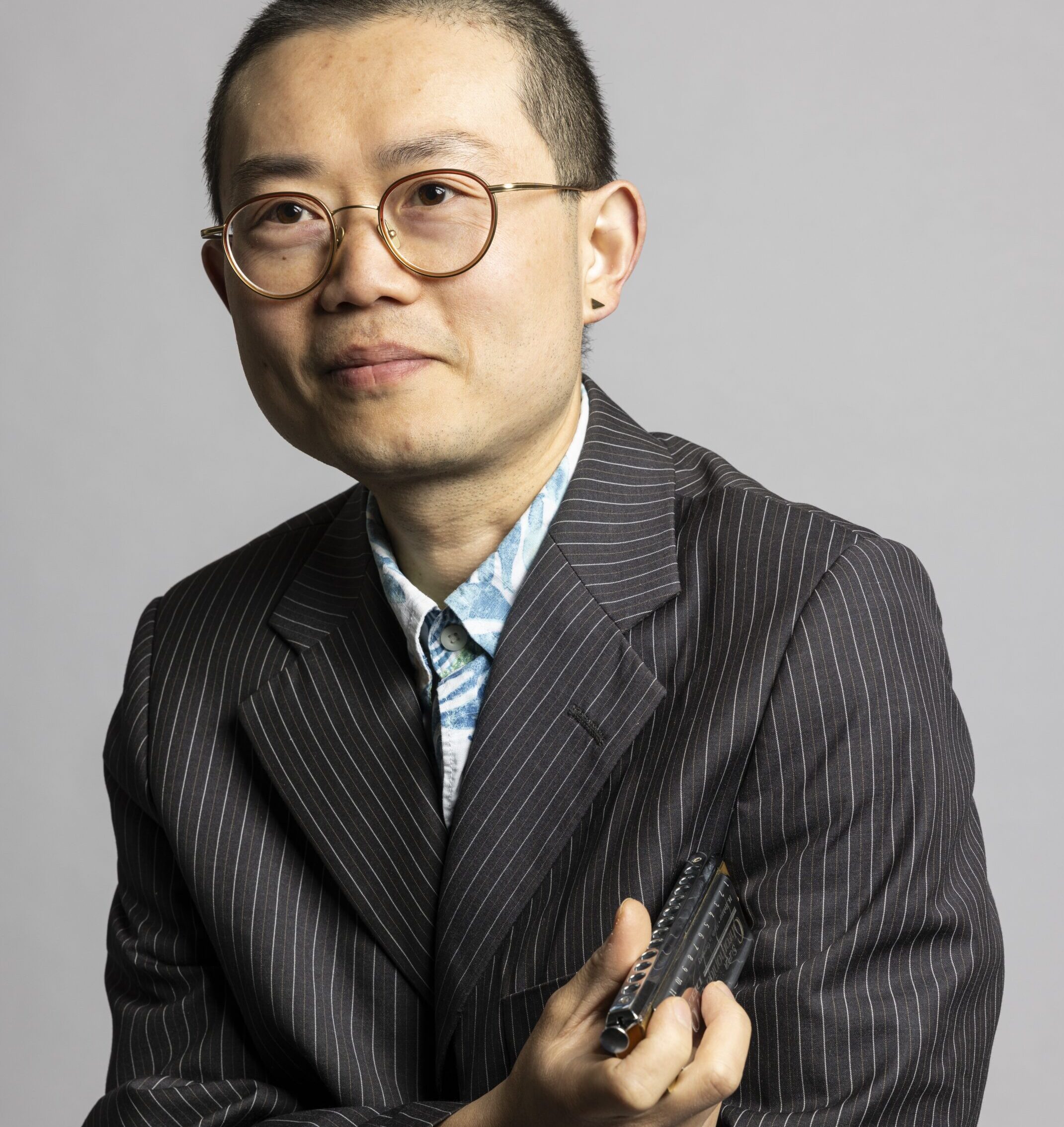 Musiker und Dozent Tian Long Li der einen gestreiften anzug trägt und in der Hand eine Mundharmocika hält